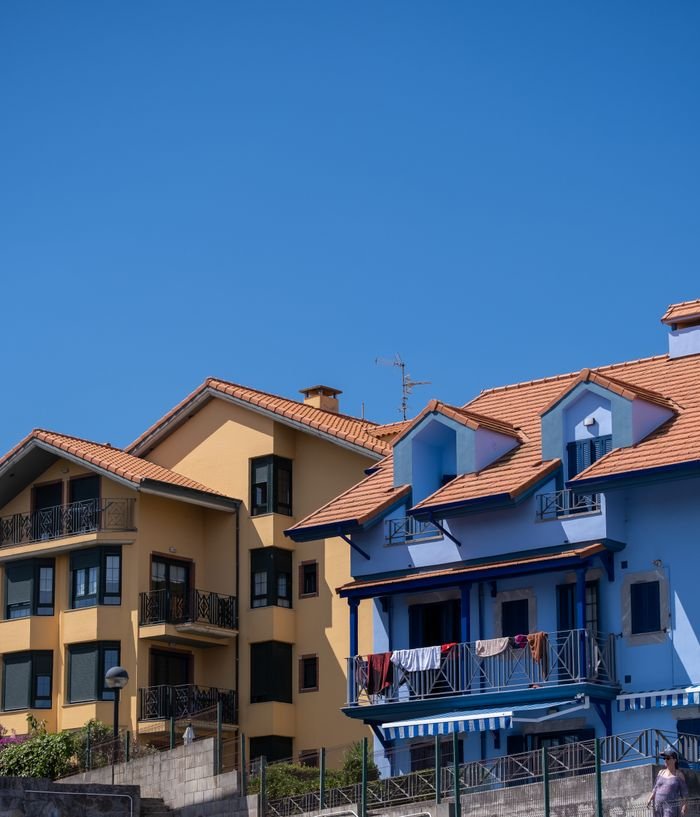 Vibrant yellow and blue suburban houses with red roofs against a clear sky, depicting modern residential architecture.